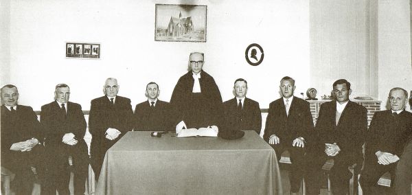 Ter gelegenheid van het afscheid van ds. M. Verweij op 1 oktober 1961 maakt fotograaf Ies Lamain een foto van de kerkenraad van de Hervormde gemeente in de nieuwe consistoriekamer. V.l.n.r. de ouderlingen Joos Oreel, Lieven Meulmeester, Jacob van Belzen en Klaas van de Ketterij, ds. M. Verweij, de diakenen Jan de Klerk, Cornelis Meulmeester, Dingenis van Belzen en Marinus van de Ketterij.